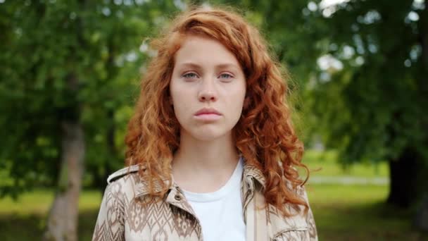 严重的青少年红发女孩看着相机站在户外在公园 — 图库视频影像