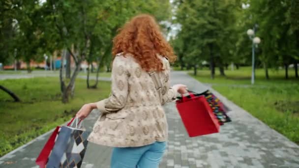 Zeitlupe eines hübschen Mädchens, das sich mit lächelnden Einkaufstüten im Park dreht — Stockvideo