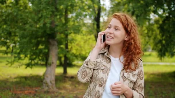 Cámara lenta de alegre adolescente riendo hablando en el teléfono móvil en el parque — Vídeos de Stock