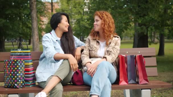 Fröhliche junge Frauen plaudern lachend entspannt draußen auf Bank im Park — Stockvideo