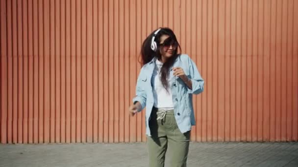 ヘッドフォンを着用して屋外でジャンプする幸せなアジアの女性のスローモーション — ストック動画