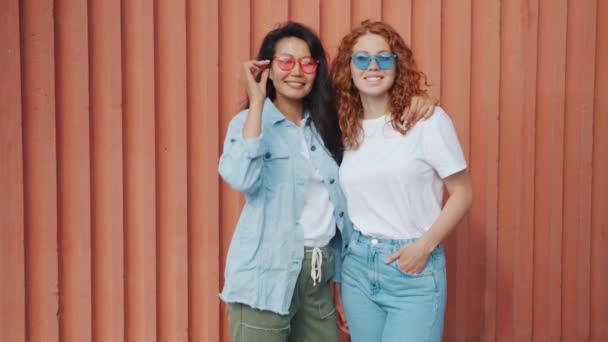 Portret van mooie meisjes vrienden staande buitenshuis dragen zonnebril glimlachend — Stockvideo