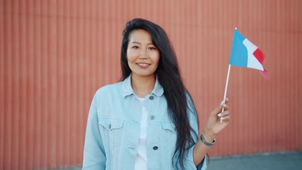 Retrato de una hermosa mujer asiática sosteniendo la bandera francesa al aire libre sonriendo — Vídeos de Stock