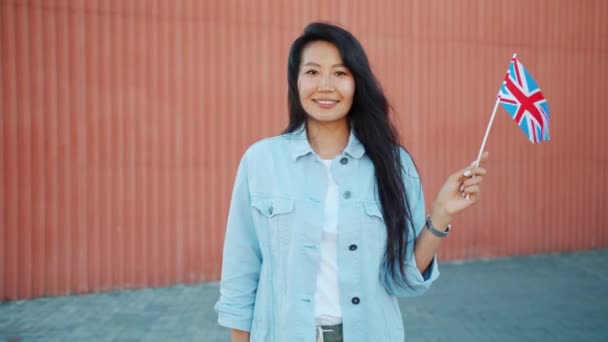 Câmera lenta de bonito asiático senhora segurando britânico bandeira sorrindo olhando para a câmera — Vídeo de Stock