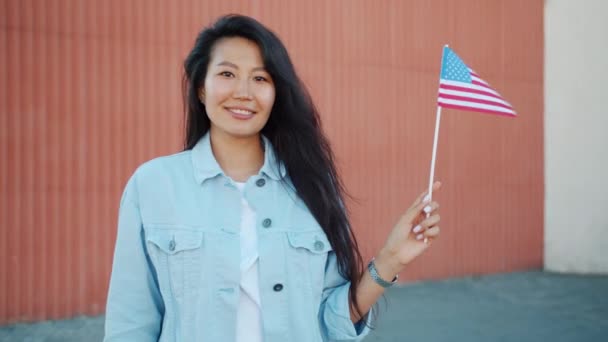 Portrait of pretty Asian girl holding US flag outdoors smiling looking at camera — Stock Video