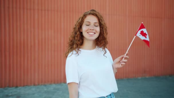 Mooie redhead tiener zwaaiende Canadese vlag buitenshuis kijken naar camera — Stockvideo