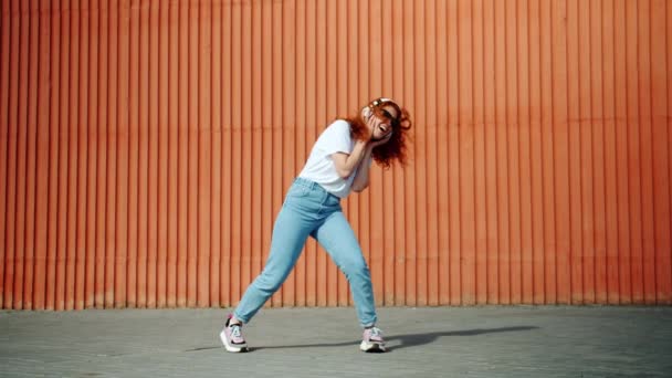 Cool estudiante chica bailando al aire libre con auriculares y gafas de sol — Vídeo de stock