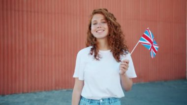 İngiliz bayrağı tutan güzel kızıl kız kamera bakarak gülümseyerek açık havada
