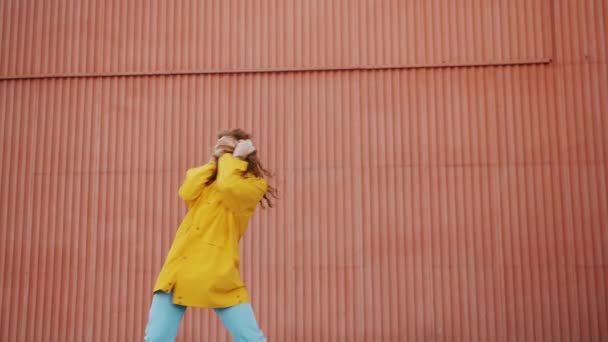 Portret van grappig meisje in regenjas dansen buitenshuis genieten van muziek in een koptelefoon — Stockvideo