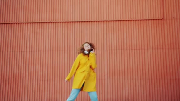 Zeitlupe eines glücklichen Teenagers im Regenmantel, der draußen gegen eine Wand tanzt — Stockvideo