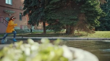 Yağmurluk ve sakız botları içinde su birikintileri içinde çalışan kız eğlenmek kulaklık giyiyor