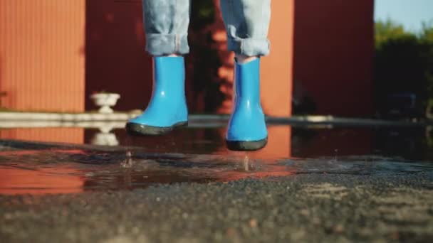 Movimiento lento de pies en botas de goma saltando en la piscina divirtiéndose en el día de otoño — Vídeos de Stock