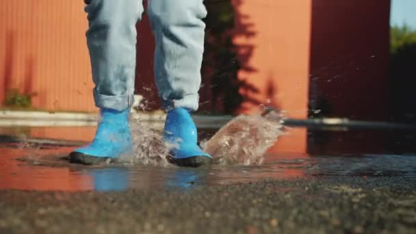 Patas femeninas en botas de goma saltando en charco en el suelo disfrutando del otoño — Vídeos de Stock