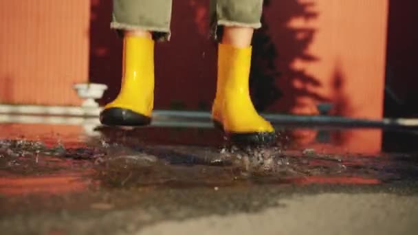 Close-up of female feet in bright rubber boots jumping in puddle outdoors — Stock Video