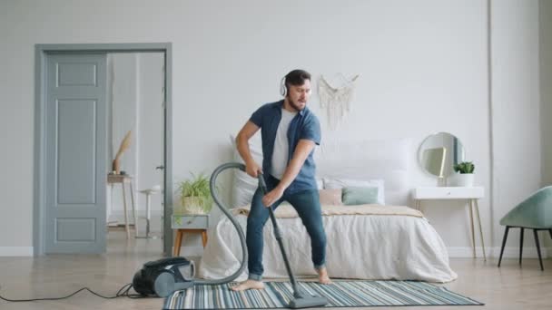 Медленное движение смешного парня пылесосит пол дома весело танцуя — стоковое видео