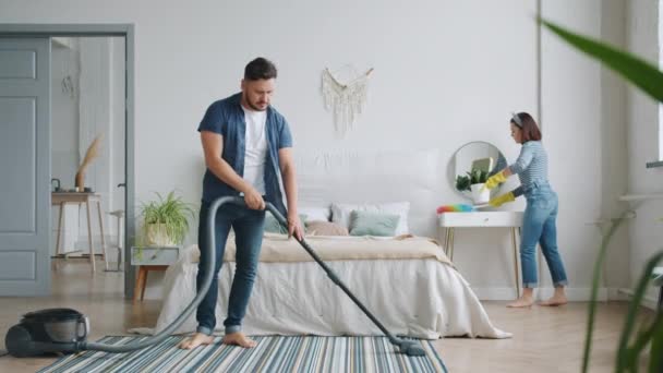 Uomo e donna impegnati con i lavori domestici in camera da letto camera di pulizia con aspirapolvere — Video Stock