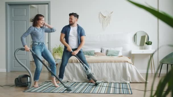 Meisje en jongen stofzuigen tapijt in slaapkamer lachen hebben plezier tijdens het opruimen — Stockvideo