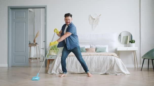 Morena sorridente em luvas de borracha lavando o chão com esfregona de plástico dançando em casa — Vídeo de Stock