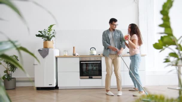 Menina e cara dançando com esfregona e espanador fazendo tarefas domésticas na cozinha — Vídeo de Stock