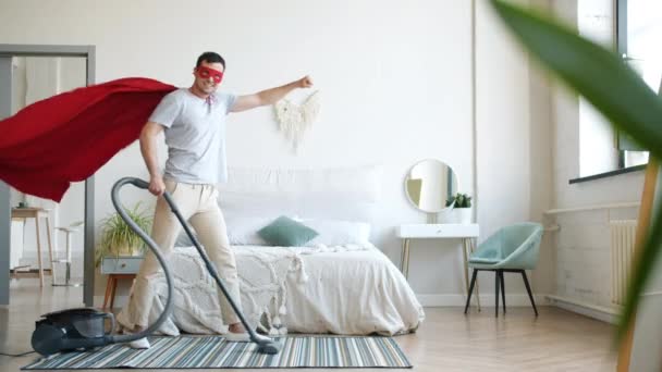 Retrato de super-homem sorridente aspirando tapete em casa e olhando para a câmera — Vídeo de Stock