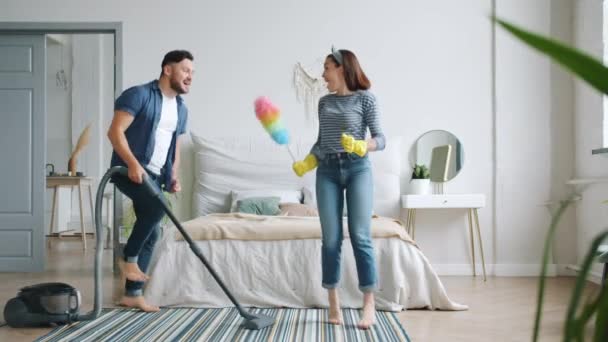 Gioiosa giovane famiglia che fa i lavori domestici cantando in spolverata e ballando insieme — Video Stock