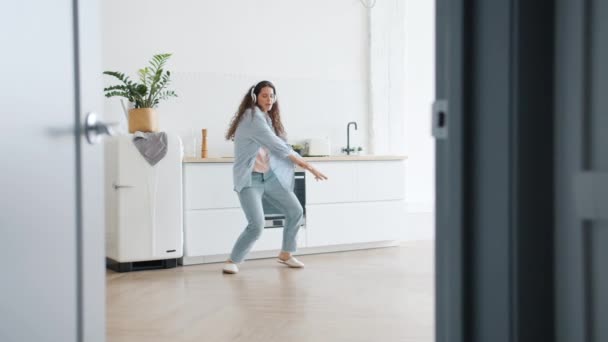 Chica divertida con pelo rizado bailando en la cocina cantando y escuchando música — Vídeos de Stock