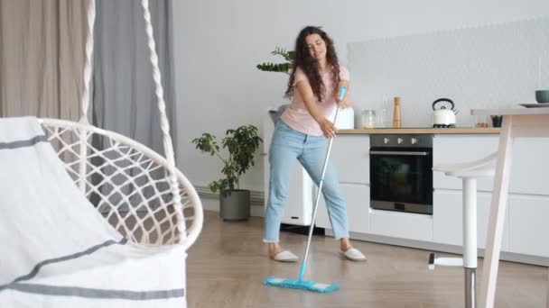 Vidám nő táncol felmosóronggyal takarítás közben a konyhában szórakozás egyedül — Stock videók