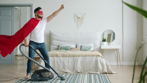 Superhero wearing red cape and mask holding vacuum cleaner in bedroom — Stock Video