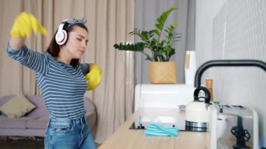 Kulaklıklı kız şarkı söyleyip dans ediyor sonra da eldiven takıp mutfağı temizliyor.