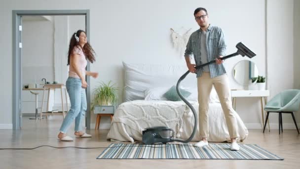 Man en vrouw dansen genieten van muziek reinigen huis met stofzuiger — Stockvideo