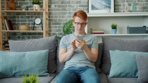 Alegre adolescente usando teléfono inteligente relajante en el sofá en casa disfrutando de gadget — Vídeo de stock
