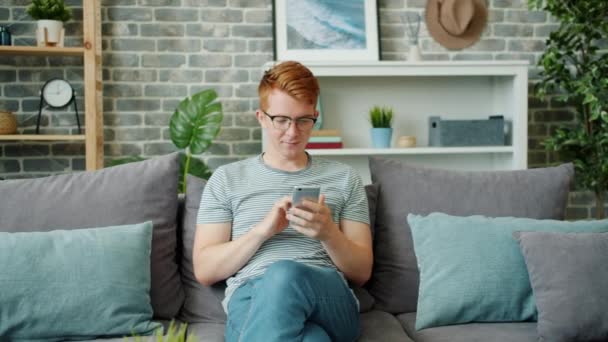 Movimento lento de menino adolescente feliz desfrutando de mídia social usando smartphone em casa — Vídeo de Stock