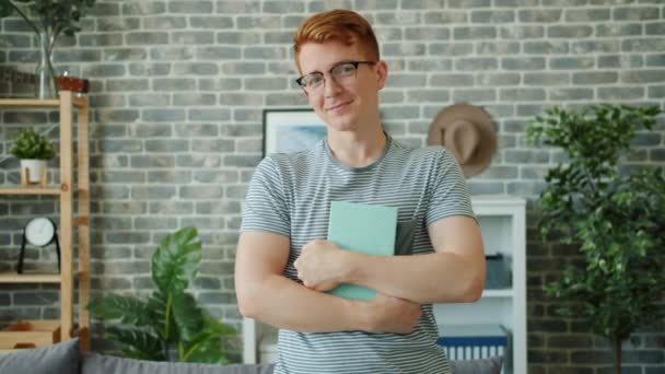 Slow motion of happy teenager in glasses holding book laughing at home — Stock Video