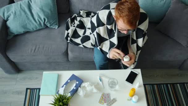 Blick aus der Vogelperspektive auf kranken jungen Mann, der zu Hause auf der Couch Tabletten trinkt — Stockvideo