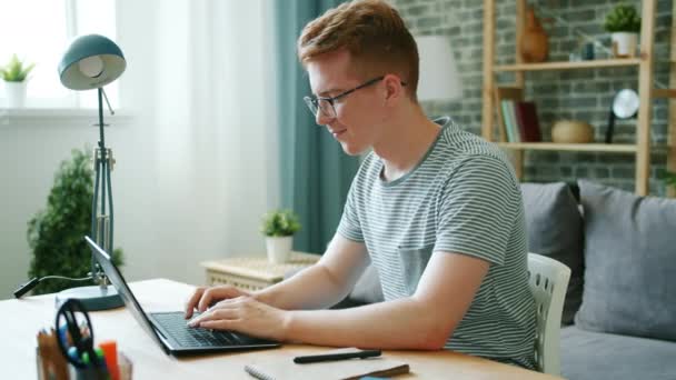 Nastoletni wolny strzelec pracujący z laptopem w domu wpisujący uśmiech na biurku — Wideo stockowe