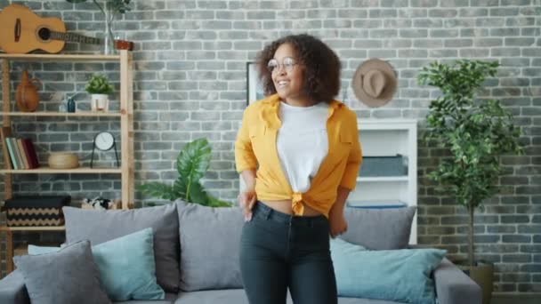 Jovencita alegre en gafas bailando en casa sola divirtiéndose con música favorita — Vídeo de stock