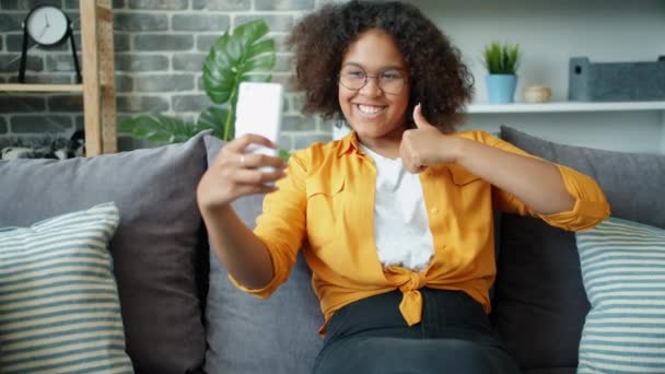 Ευτυχισμένος Αφρο-Αμερικανός έφηβος λαμβάνοντας selfie με αντίχειρες-up χειρονομία στο σπίτι — Αρχείο Βίντεο