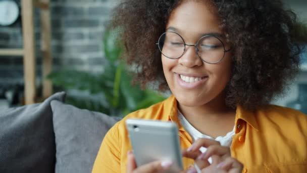 Feliz adolescente afro-americano usando smartphone em casa rindo — Vídeo de Stock