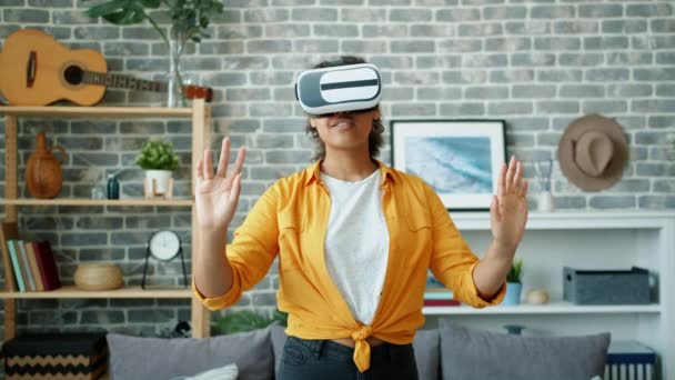 Afro-Amerikaanse vrouw in virtual reality bril bewegende armen glimlachen thuis — Stockvideo