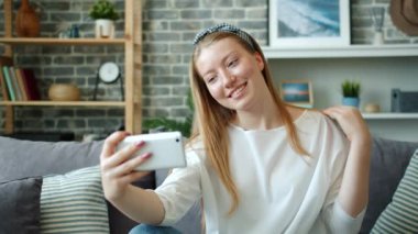 Güzel kız evinde akıllı telefon kamerasıyla saçına dokunarak selfie çekiyor.