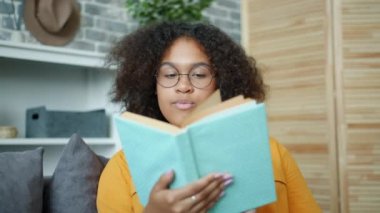 Güzel Afrikalı Amerikalı kadın evde kitap okuyor sayfaları çeviriyor gülümsüyor