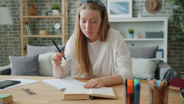 Diligente adolescente haciendo tareas de lectura de libros de escritura en el escritorio en el apartamento — Vídeos de Stock