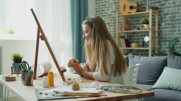 Joyful student schilderij beeld thuis, penseel en palet zichtbaar op tafel — Stockvideo