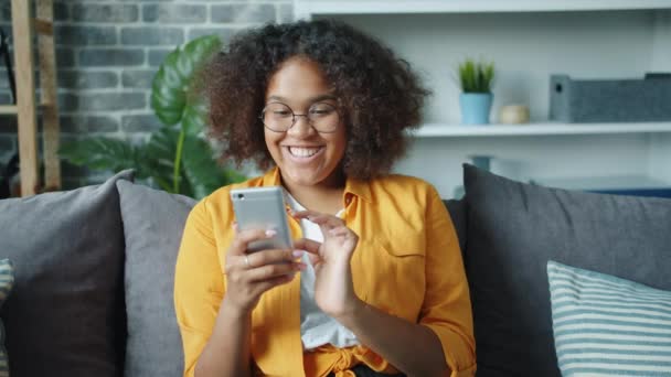 아름다운 아프리카 계 미국인 여자 아이가 스마트폰으로 집에서 쉬면서 웃는 모습 — 비디오