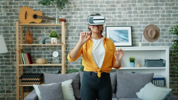Happy Afro-American girl playing game in virtual reality glasses in apartment — Stock Video