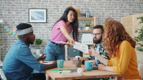 Mouvement lent de la jeune femme chef de groupe donnant des graphiques aux membres de l'équipe en fonction — Video