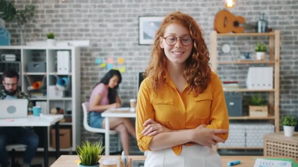 Allegro rossa donna in occhiali in piedi in ufficio con le braccia incrociate sorridente — Video Stock