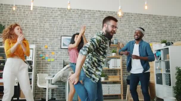Бородатий хлопець танцює в офісі, а колеги плескають руками, розважаючись разом — стокове відео