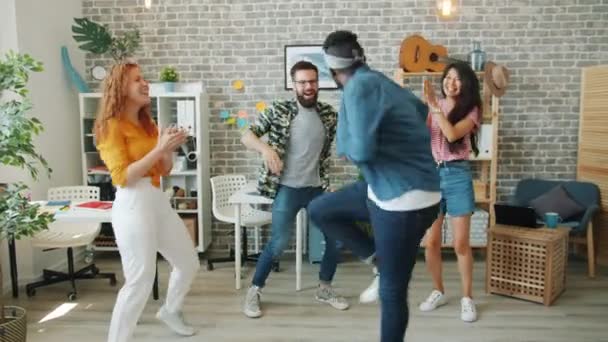 Захоплені молоді люди танцюють на корпоративній вечірці, плескаючи руками в сучасному офісі — стокове відео