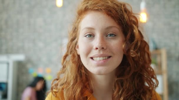 Portrait en gros plan d'une jeune femme joyeuse aux cheveux bouclés rouges souriant au bureau — Video